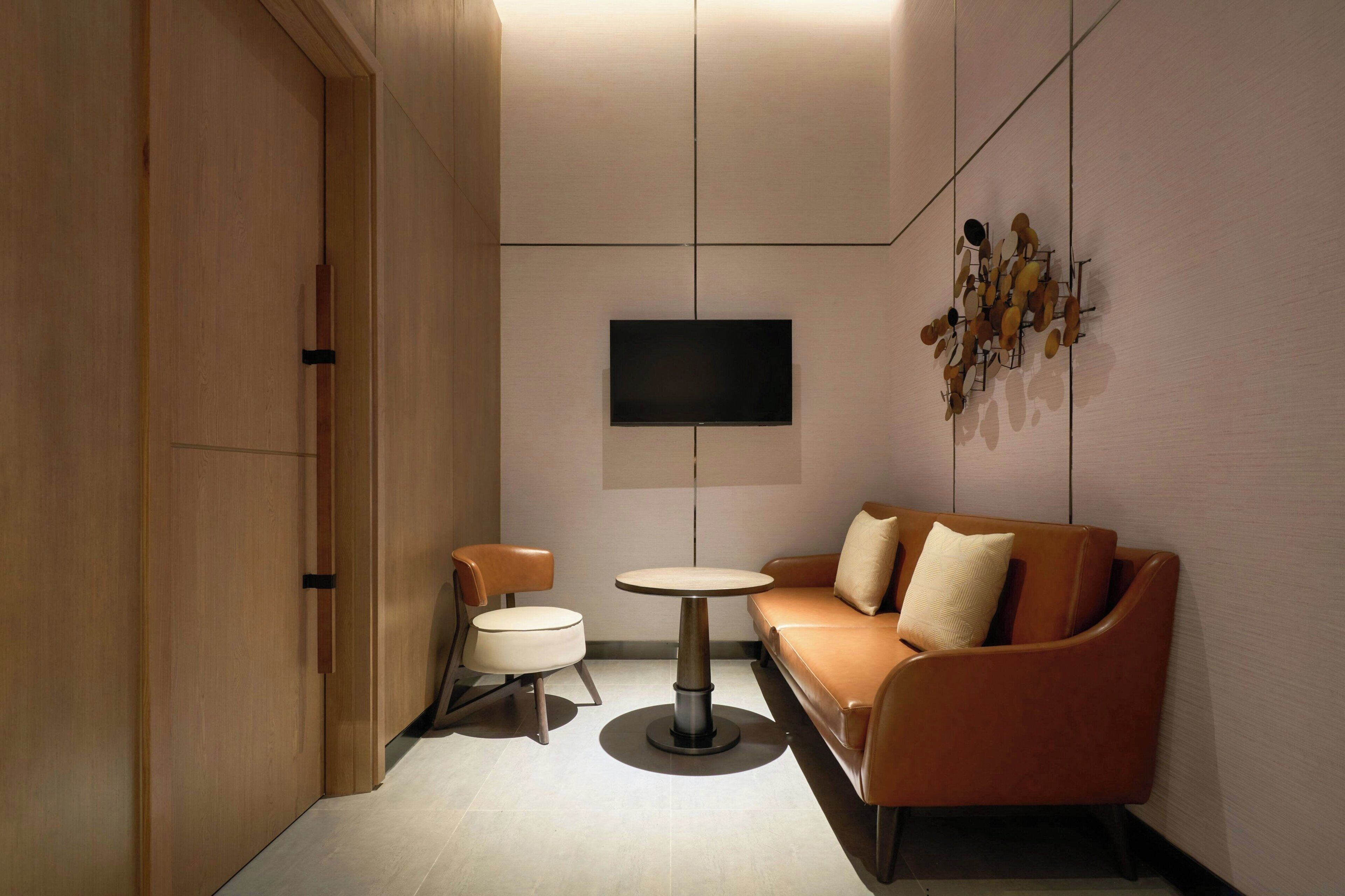 Une chambre moderne avec un canapé, une petite table ronde et un téléviseur fixé au mur.
