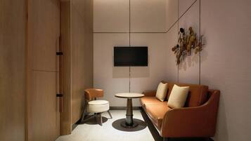 Une chambre moderne avec un canapé, une petite table ronde et un téléviseur fixé au mur.