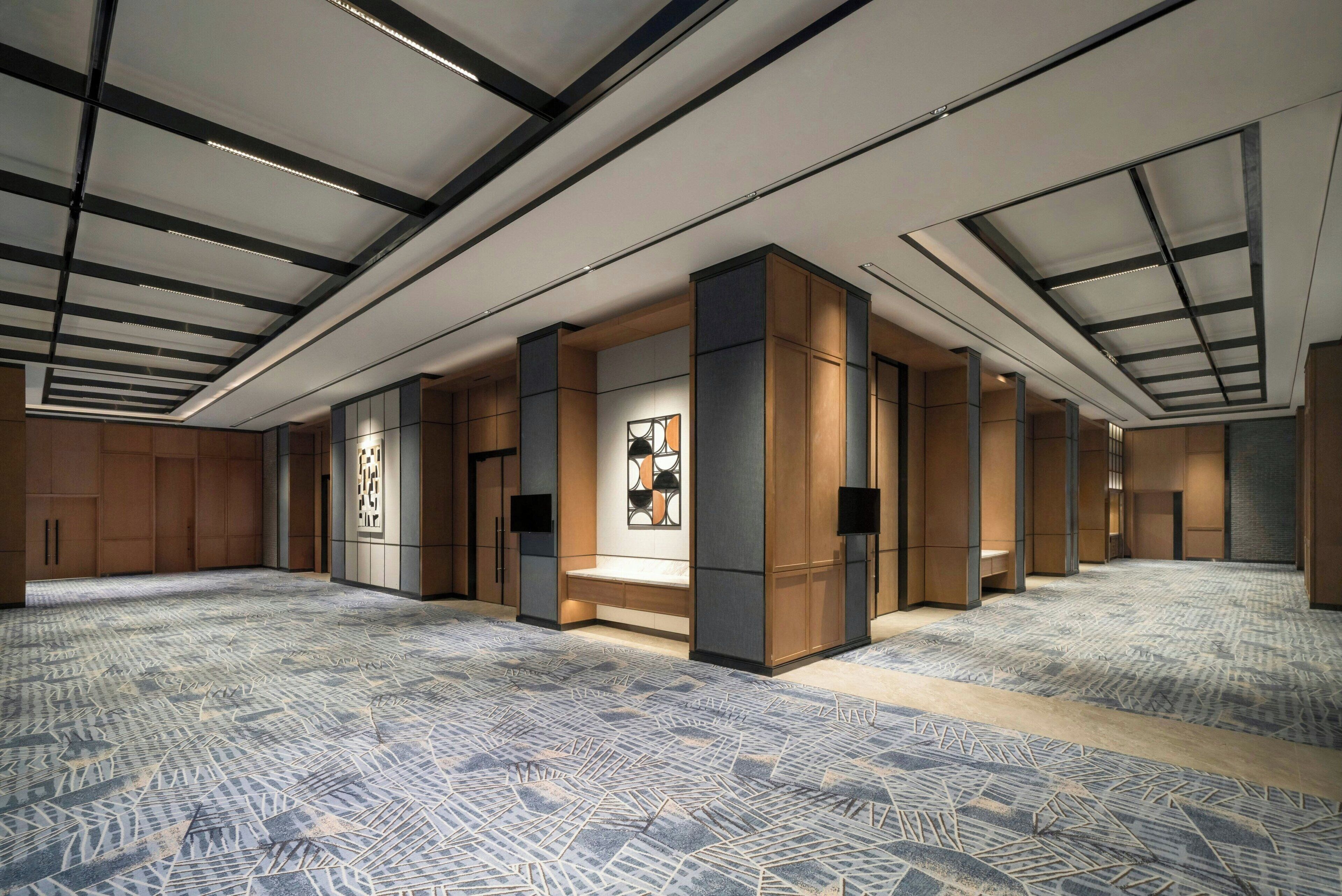 Eine großzügige Hotelhalle mit einem gemusterten Teppich, Holzwandverkleidungen und einem modernen Deckenstil.