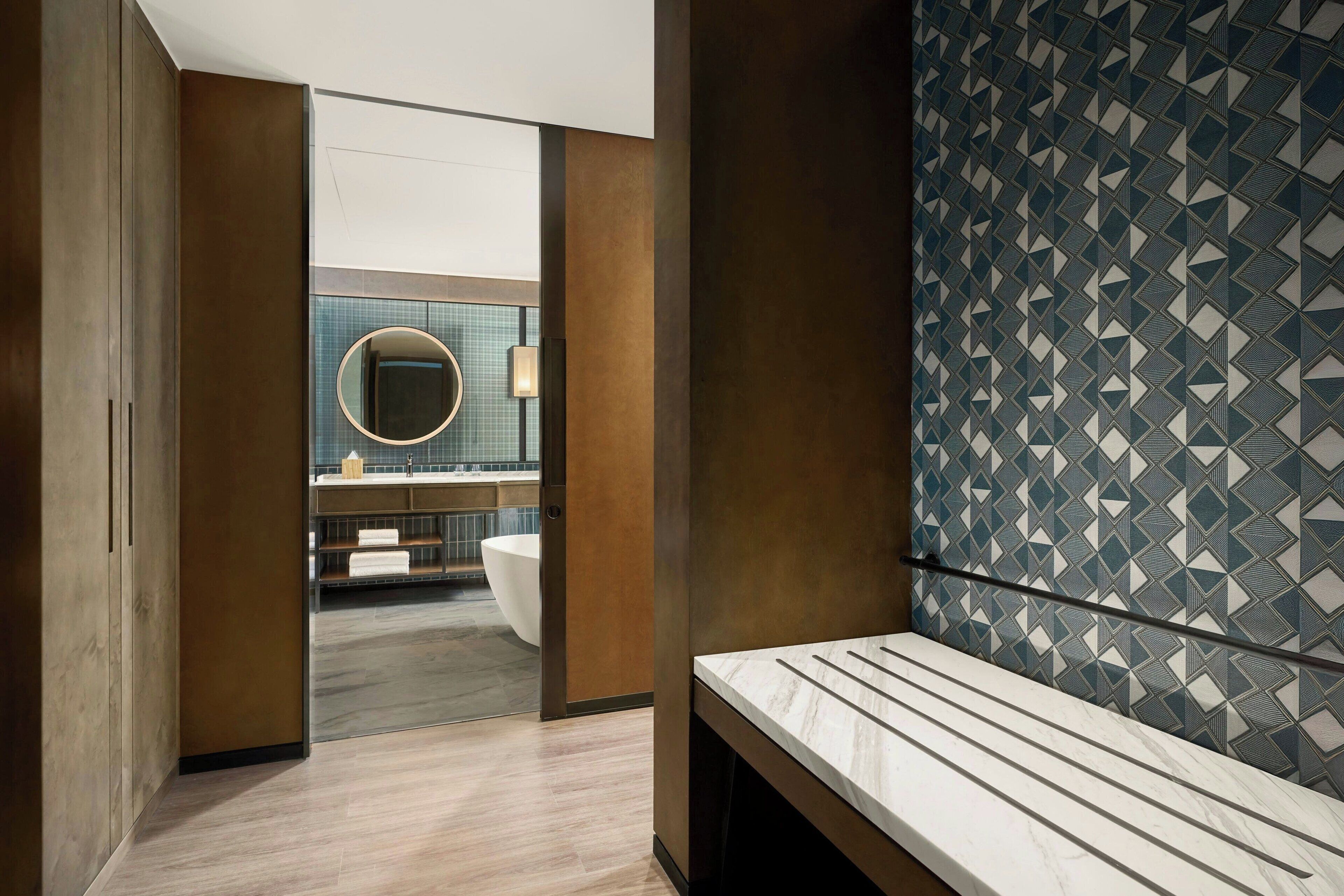 A modern bathroom with a large mirror, a bathtub, and a patterned wall.