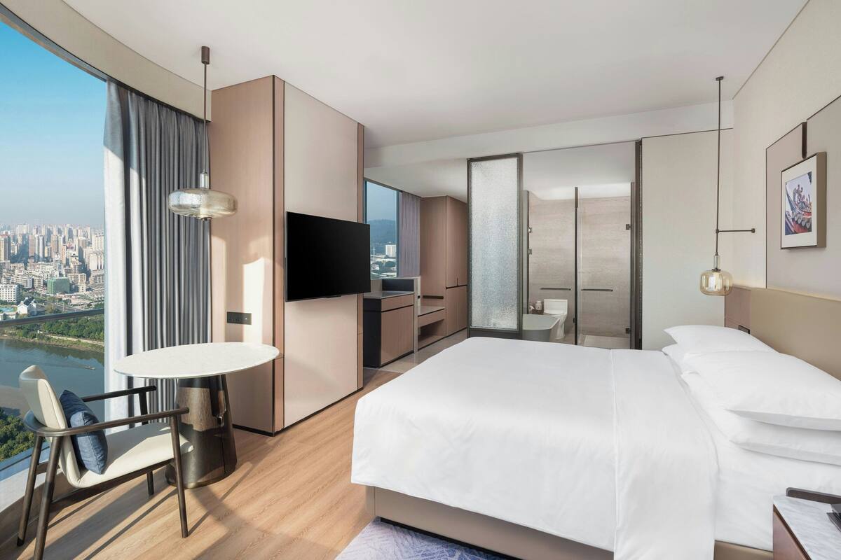 Une chambre d’hôtel moderne dotée d’un grand lit, d’une table à manger, d’une télévision et offrant une vue sur la ville.
