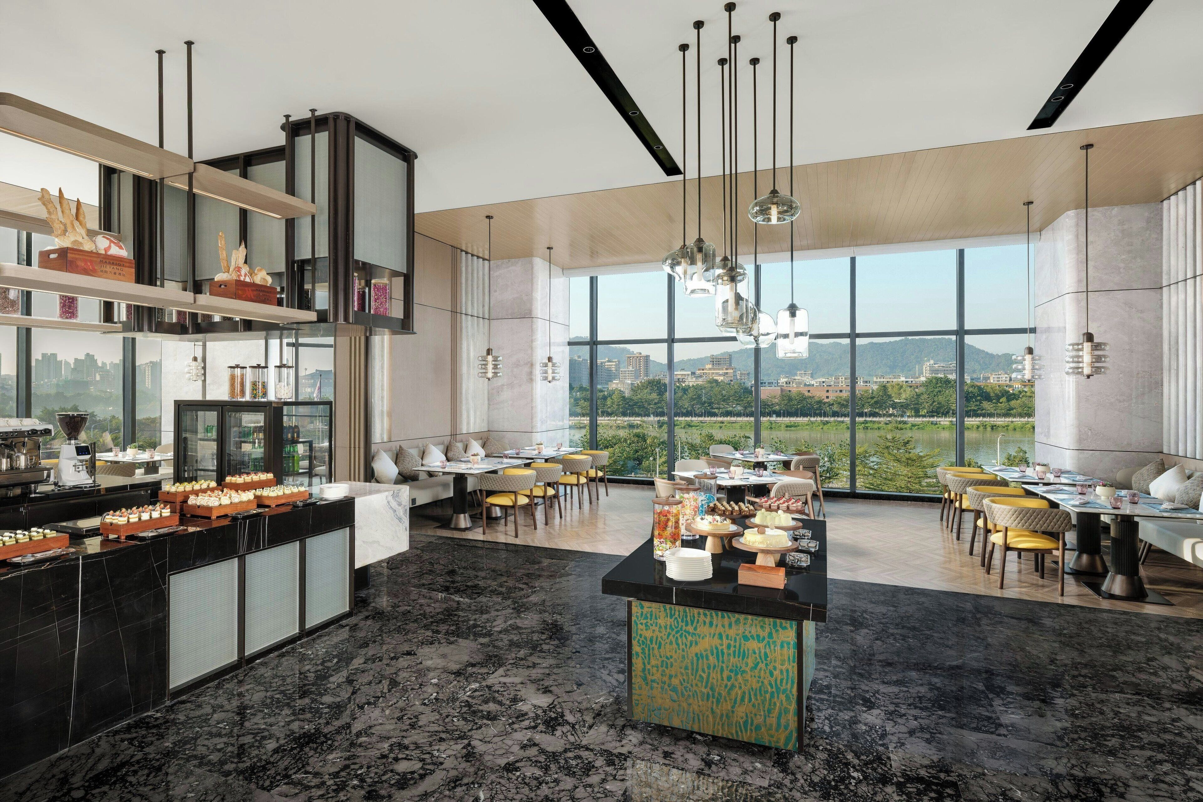 A modern dining area with a high ceiling, large windows, and a city view.