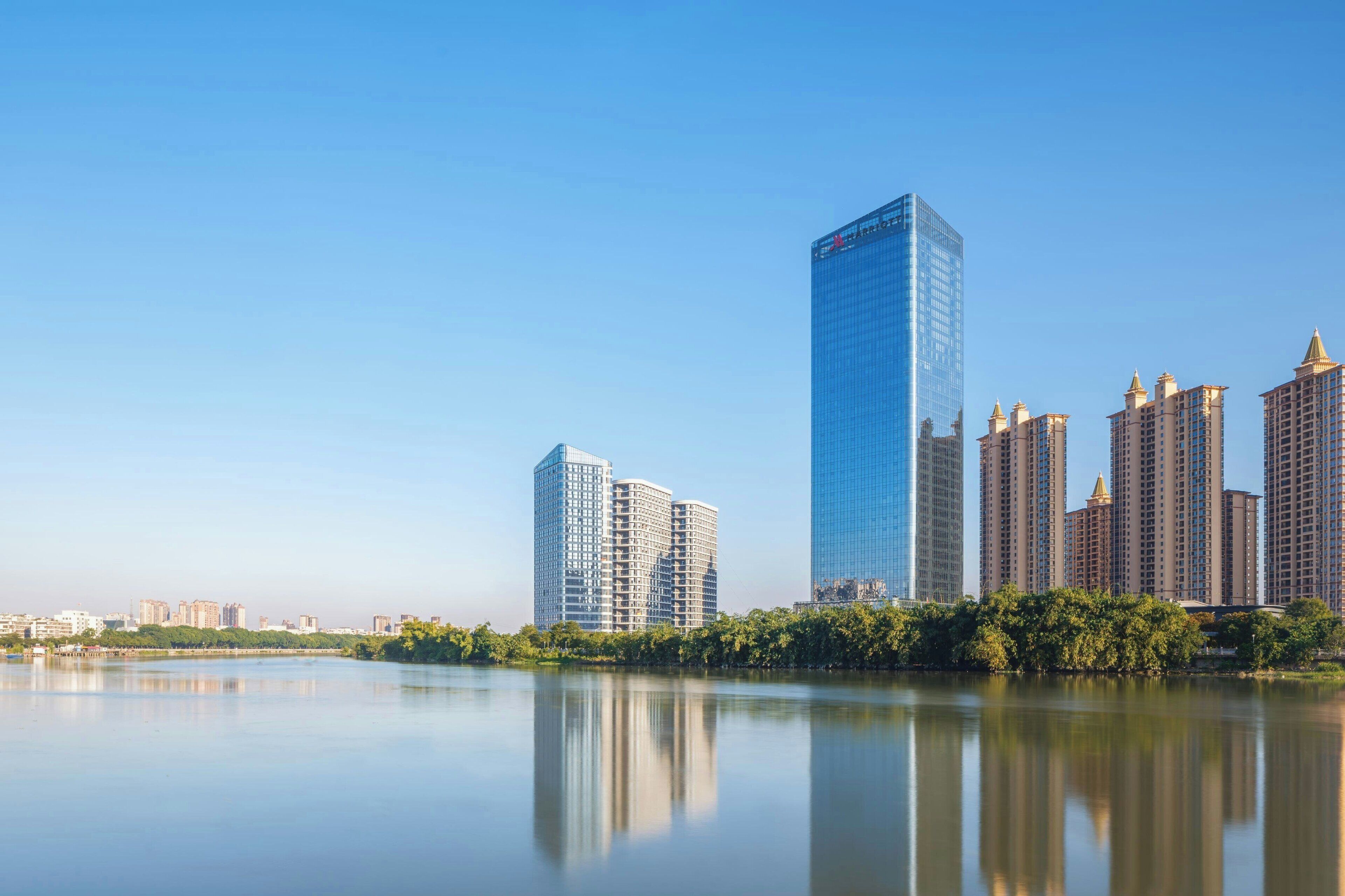 A cityscape with modern high-rise buildings, a calm body of water reflecting the structures, and a clear sky.