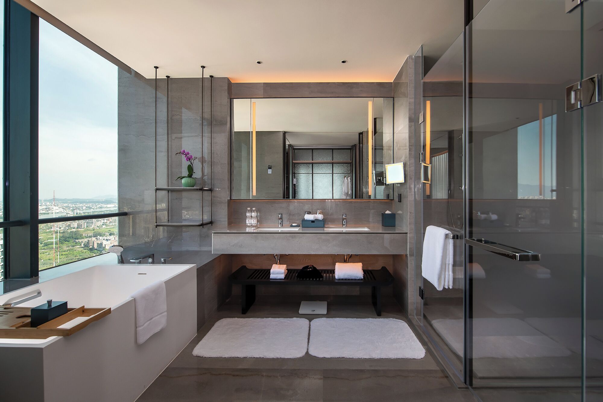 Un baño moderno con un ventanal grande, cabina de ducha de vidrio y tocador con espejo.