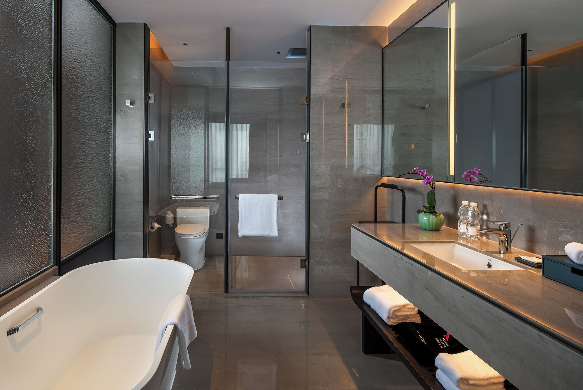 A modern bathroom with a glass-enclosed shower, a white bathtub, and a vanity with a large mirror.