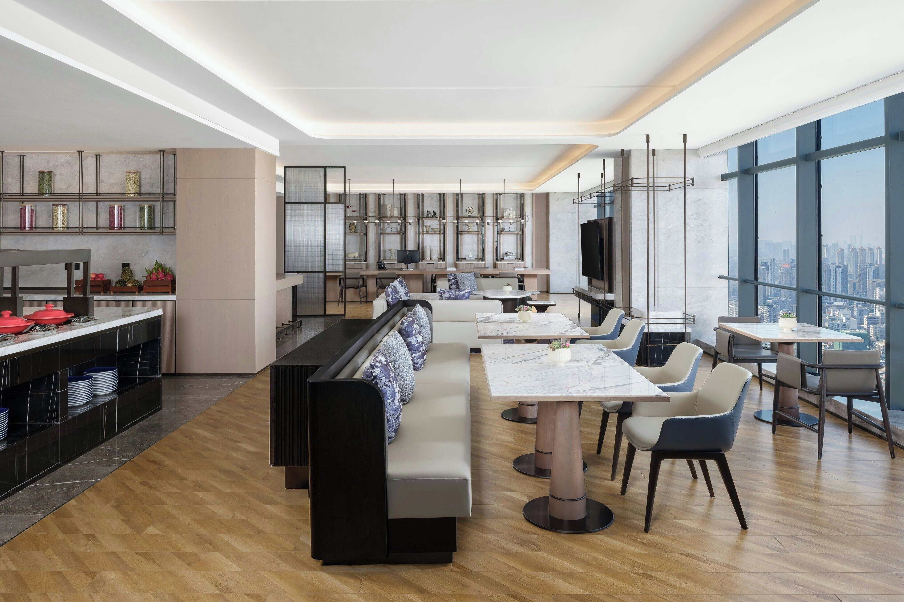 A modern restaurant with a long counter, seating area, and large windows offering a city view.