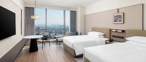 A hotel room with two beds, a TV, a small table, and a city view.
