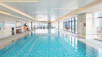 A large indoor swimming pool with clear blue water, surrounded by walls with windows and a ceiling with recessed lighting.