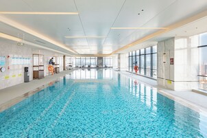 Una amplia piscina interior con agua cristalina, rodeada de paredes con ventanas e iluminación empotrada en el techo.
