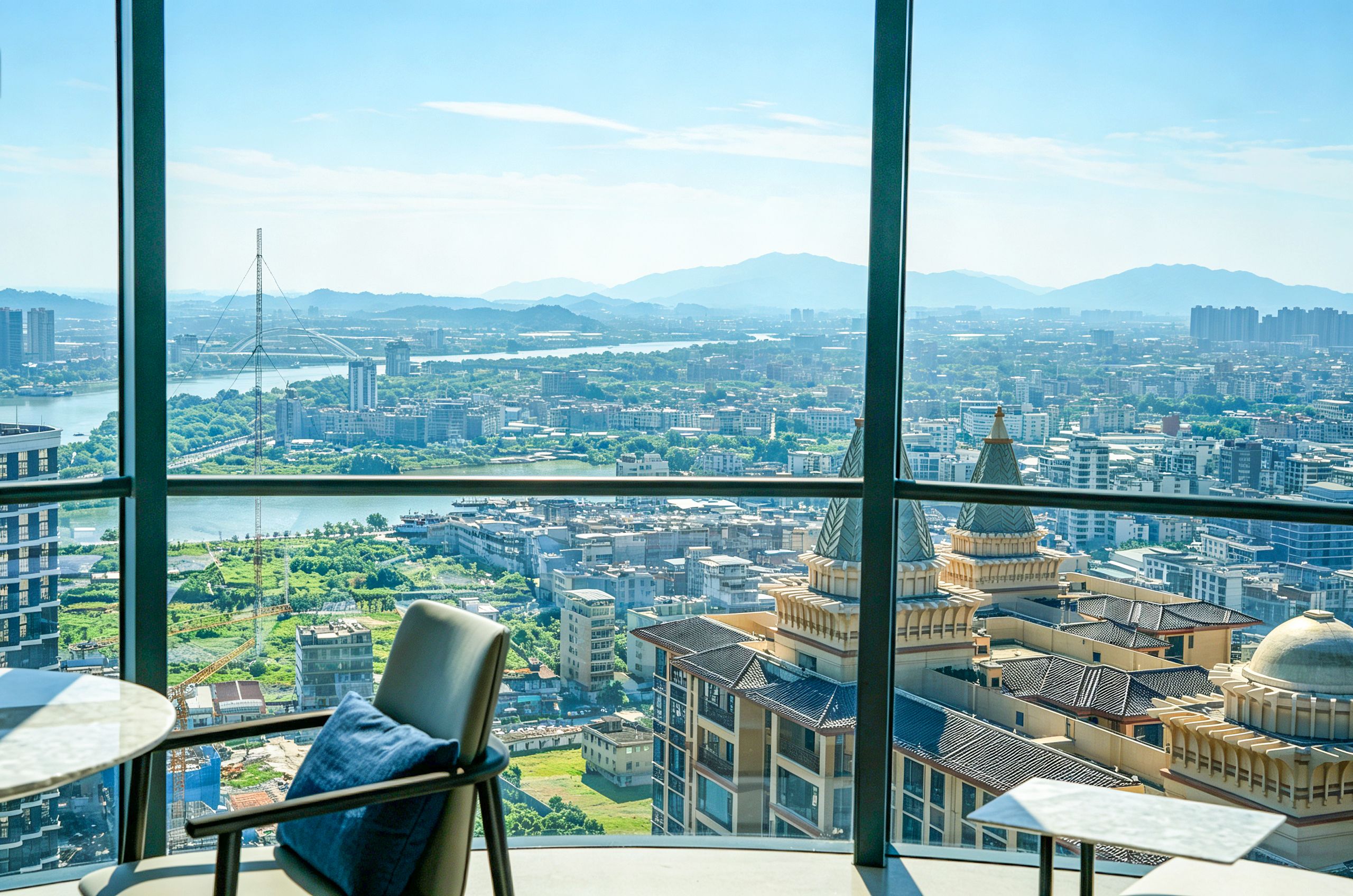 A high-rise hotel room with a panoramic city view, a chair, and a small table.