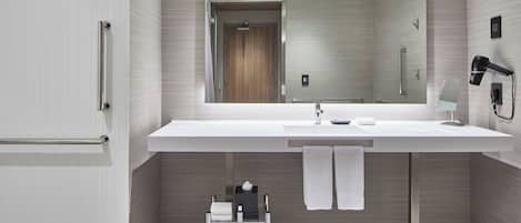Un baño moderno con un espejo grande, lavamanos blanco, toallero y secador de pelo.