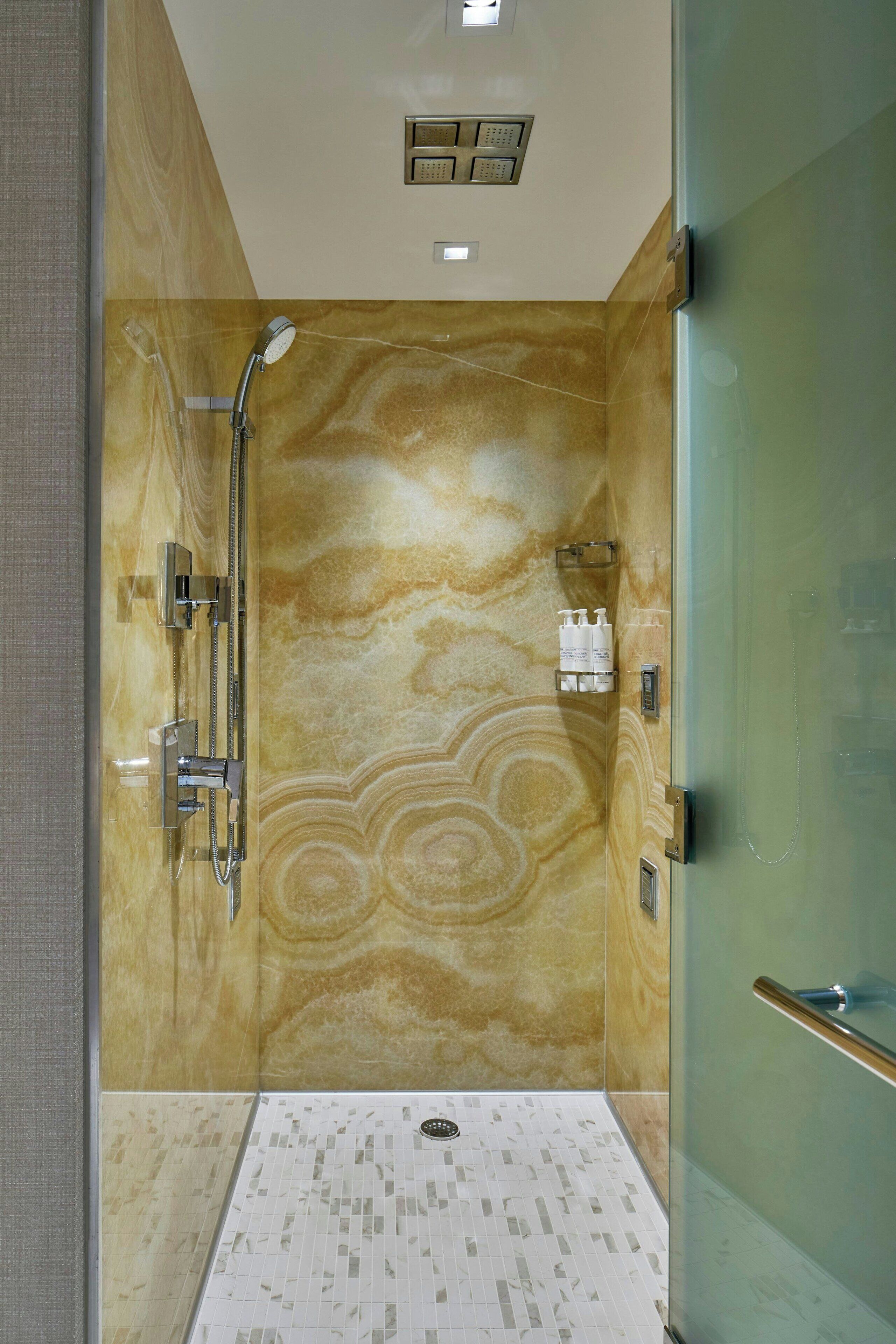 A modern shower with a glass door, a marble wall, and a tiled floor.