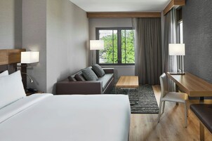 A hotel room with a bed, a sofa, a desk, and a window with curtains.