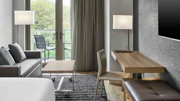 Ein modernes Hotelzimmer mit einer Couch, einem kleinen Tisch, einer Bank und Blick ins Freie durch eine Glastür.