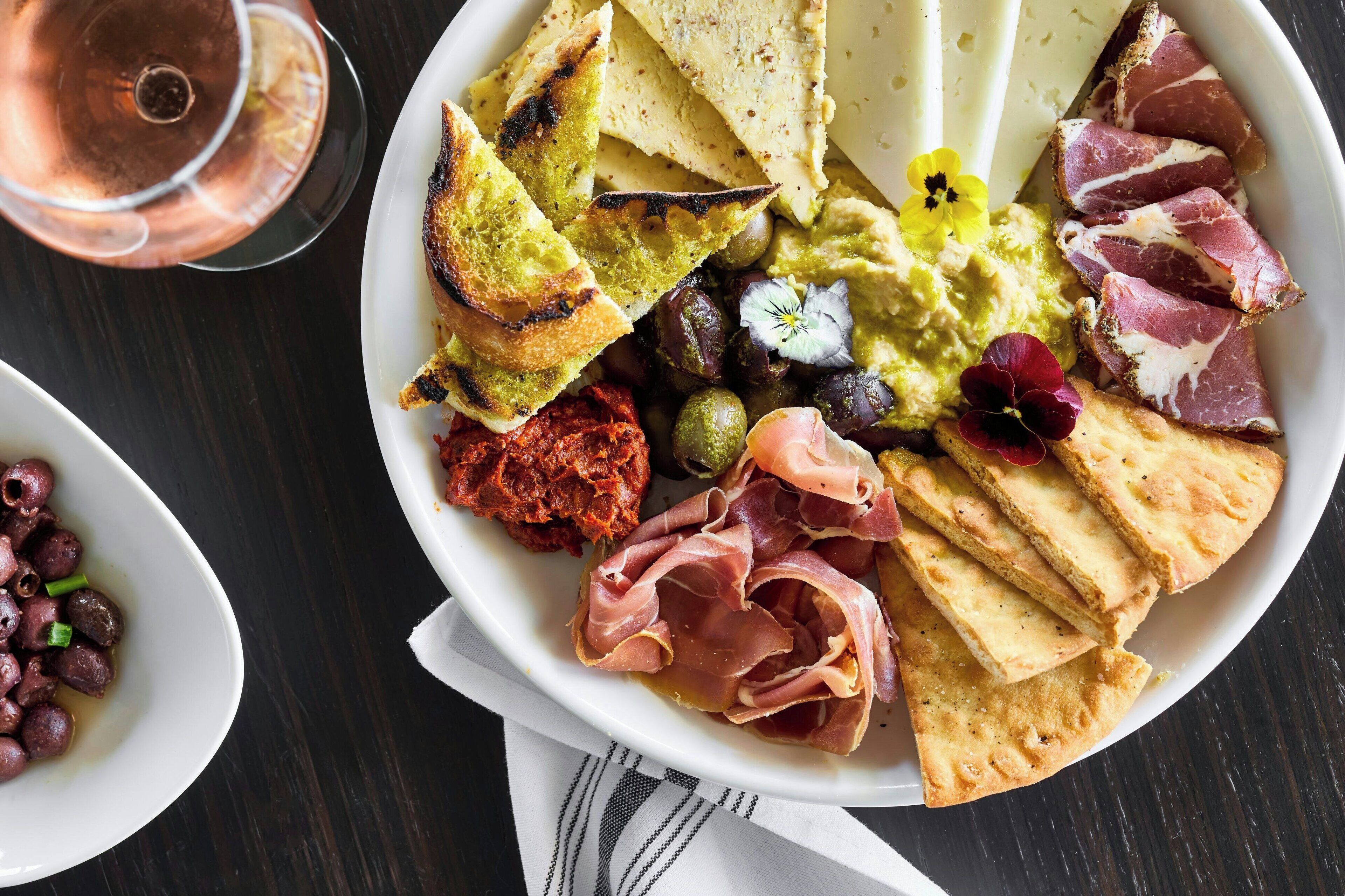 Une planche de charcuterie comprenant différentes sortes de viandes, de fromages, d’olives et du pain.