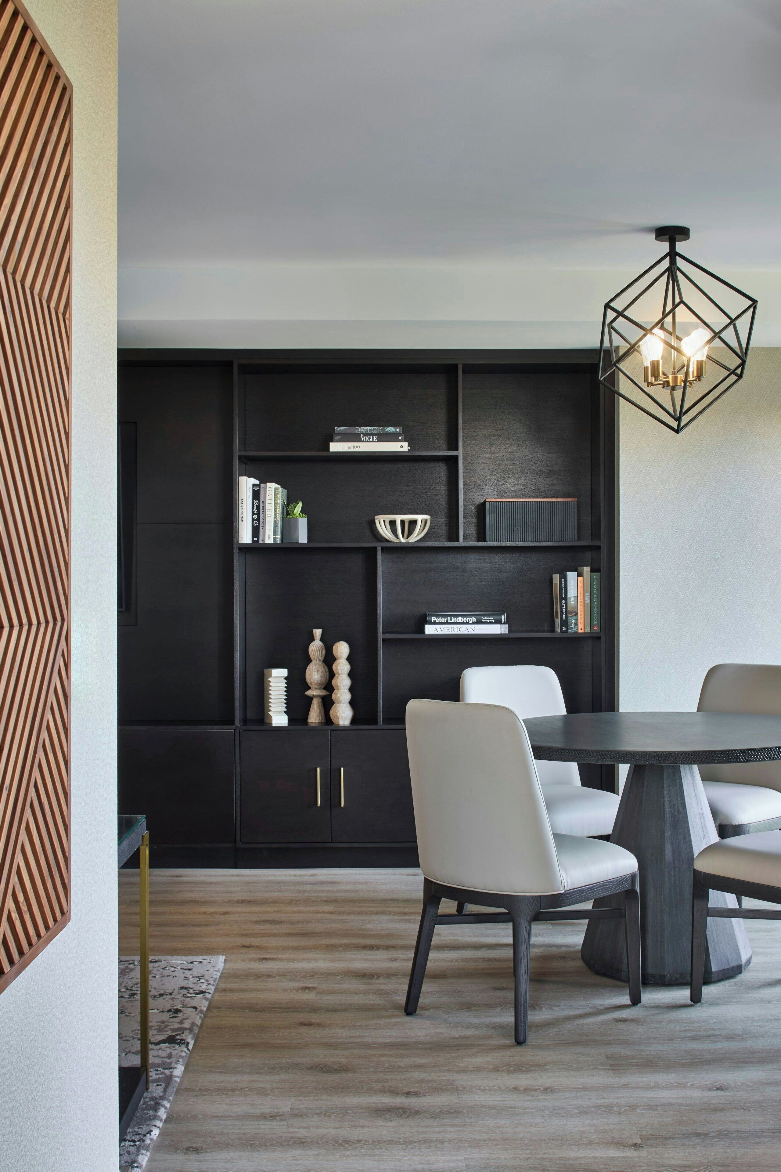 A modern dining area with a dark-colored bookshelf, white chairs, and a round table.