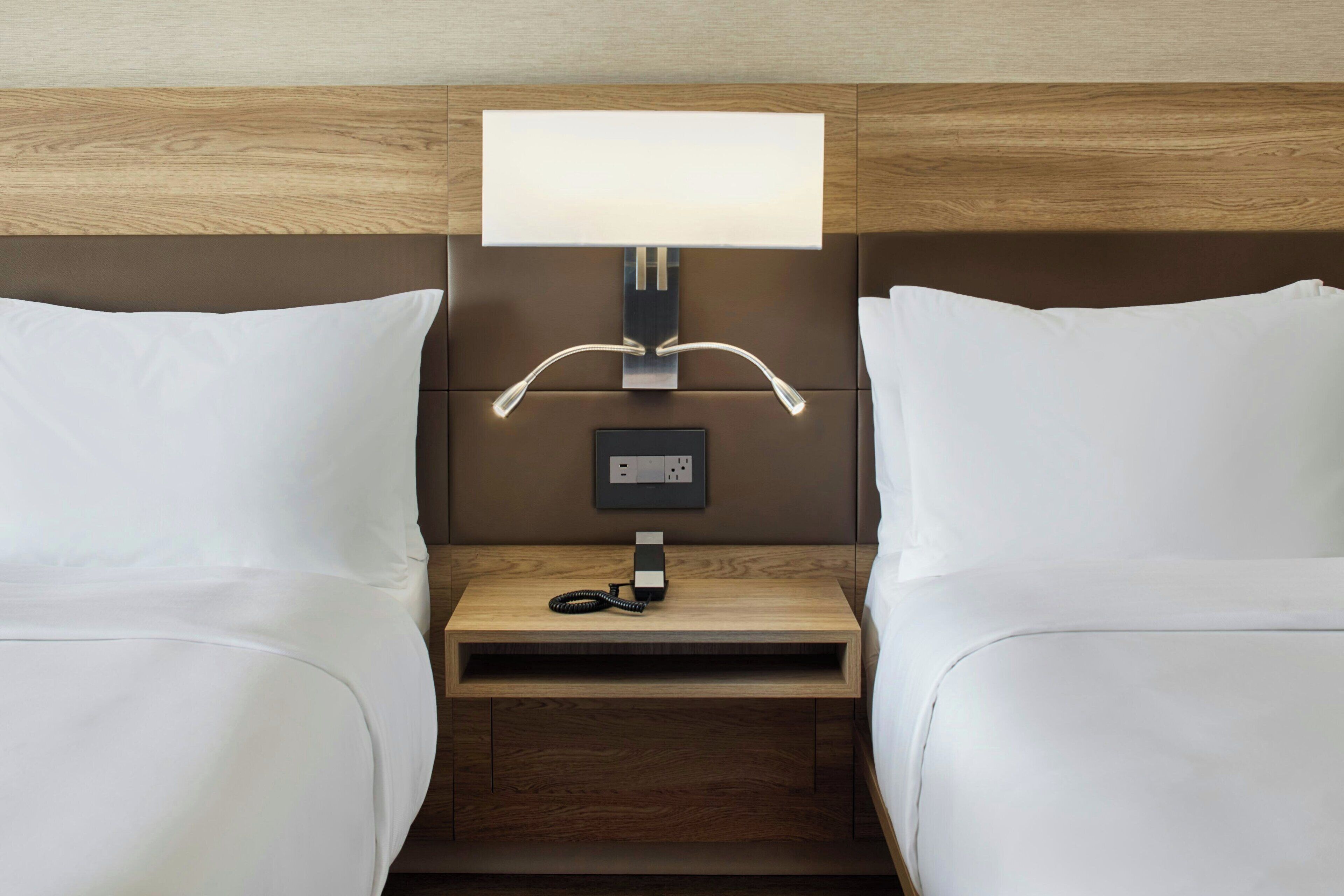Habitación de hotel con cabecera de madera, una mesita de noche con lámpara y un teléfono.