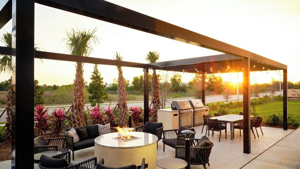 An outdoor patio with a round table, chairs, and a grill. - Towneplace Suites By Marriott Fort Myers Southeast (Fort Myers)