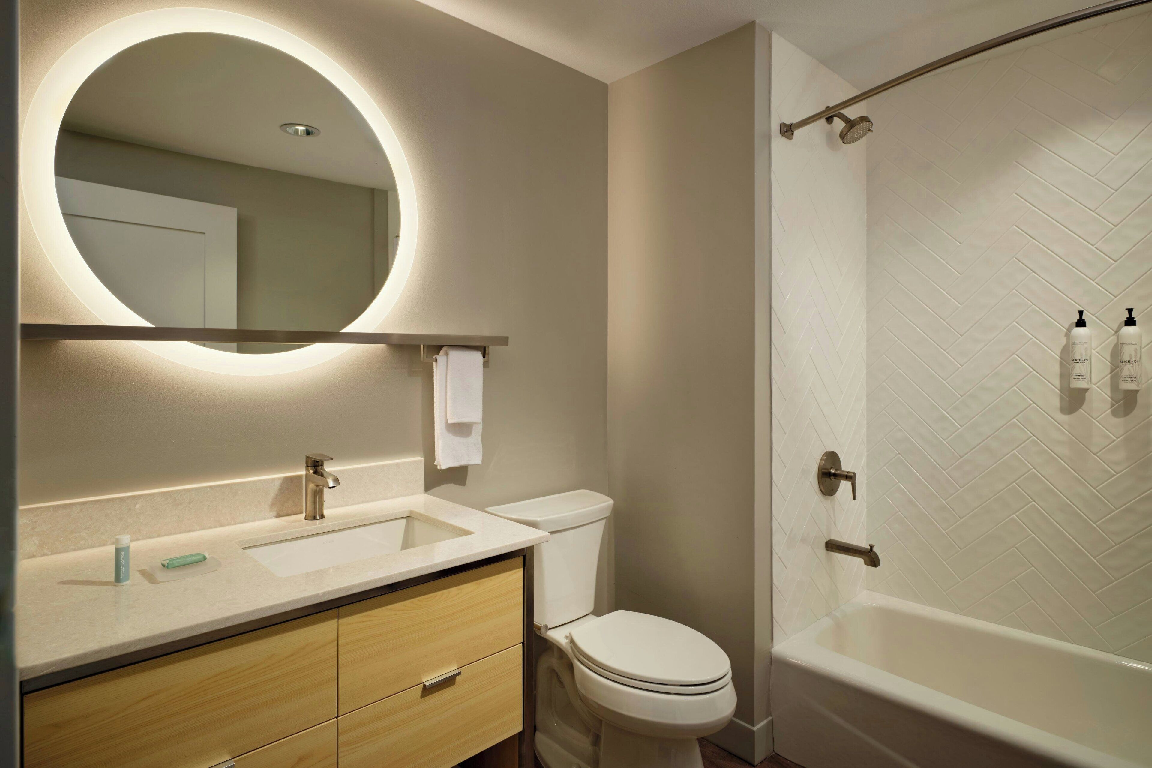 A modern bathroom with a round mirror, a sink, a toilet, and a bathtub.