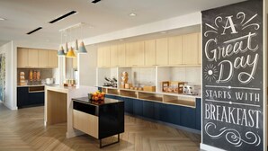A modern kitchen with wooden cabinets, a central island, pendant lights, and a chalkboard sign saying "A Great Day Starts with Breakfast". - Towneplace Suites By Marriott Fort Myers Southeast (Fort Myers)