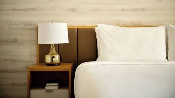 A neatly made bed with white linens and a wooden nightstand with a lamp and a book.