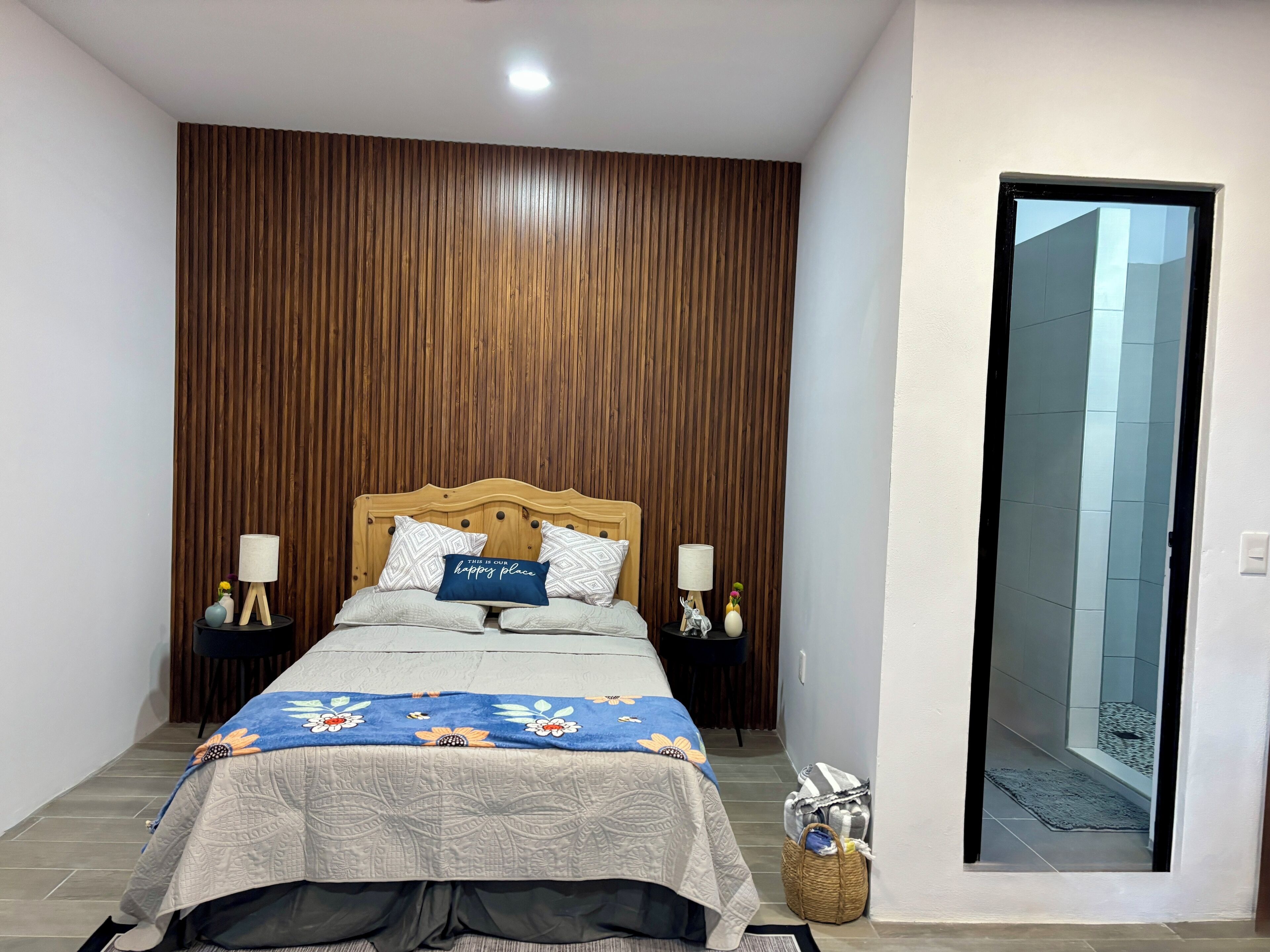 A bedroom with a wooden headboard, a bed with a floral bedspread, two bedside tables with lamps, and a small side table with decorative items.