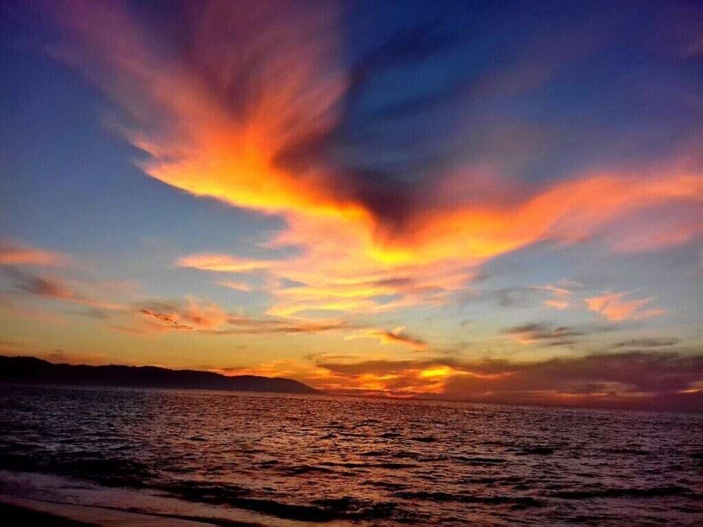 Un coucher de soleil sur une étendue d’eau, avec un ciel dégagé.