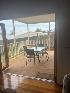 Eine überdachte Terrasse mit Tisch und Stühlen, Blick auf den Garten und Holzboden.