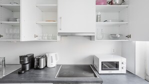 A modern kitchen with white cabinets, a black countertop, a coffee maker, a toaster, a kettle, a microwave, and a sink. - Blueground | Gundeldingen 2bd apartment (Basel)