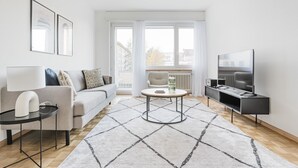 A modern living room with a sofa, coffee table, TV, and a view through large windows. - Blueground | Gundeldingen 2bd apartment (Basel)