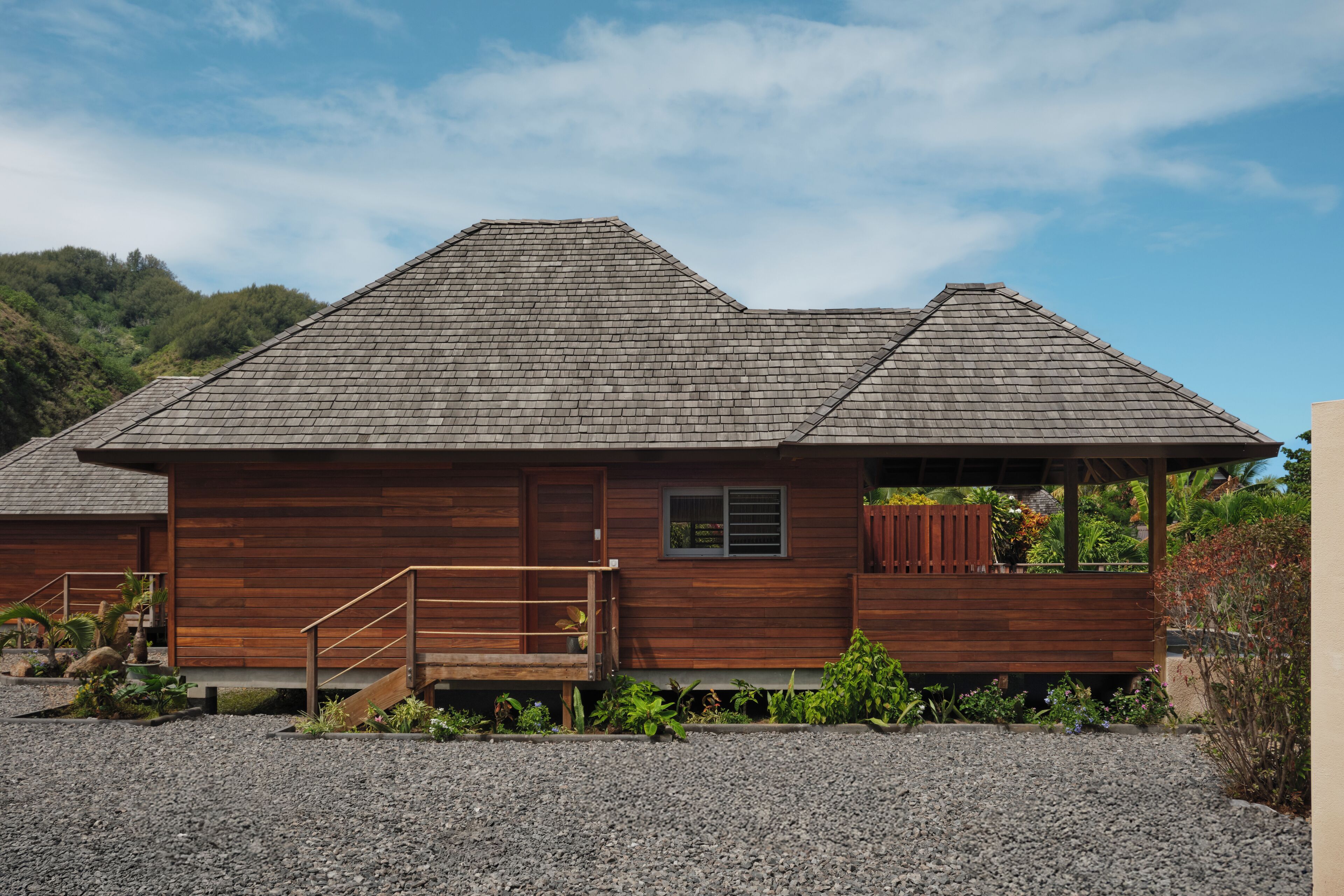 A wooden cabin with a sloped roof, a wooden deck, and a gravel driveway.