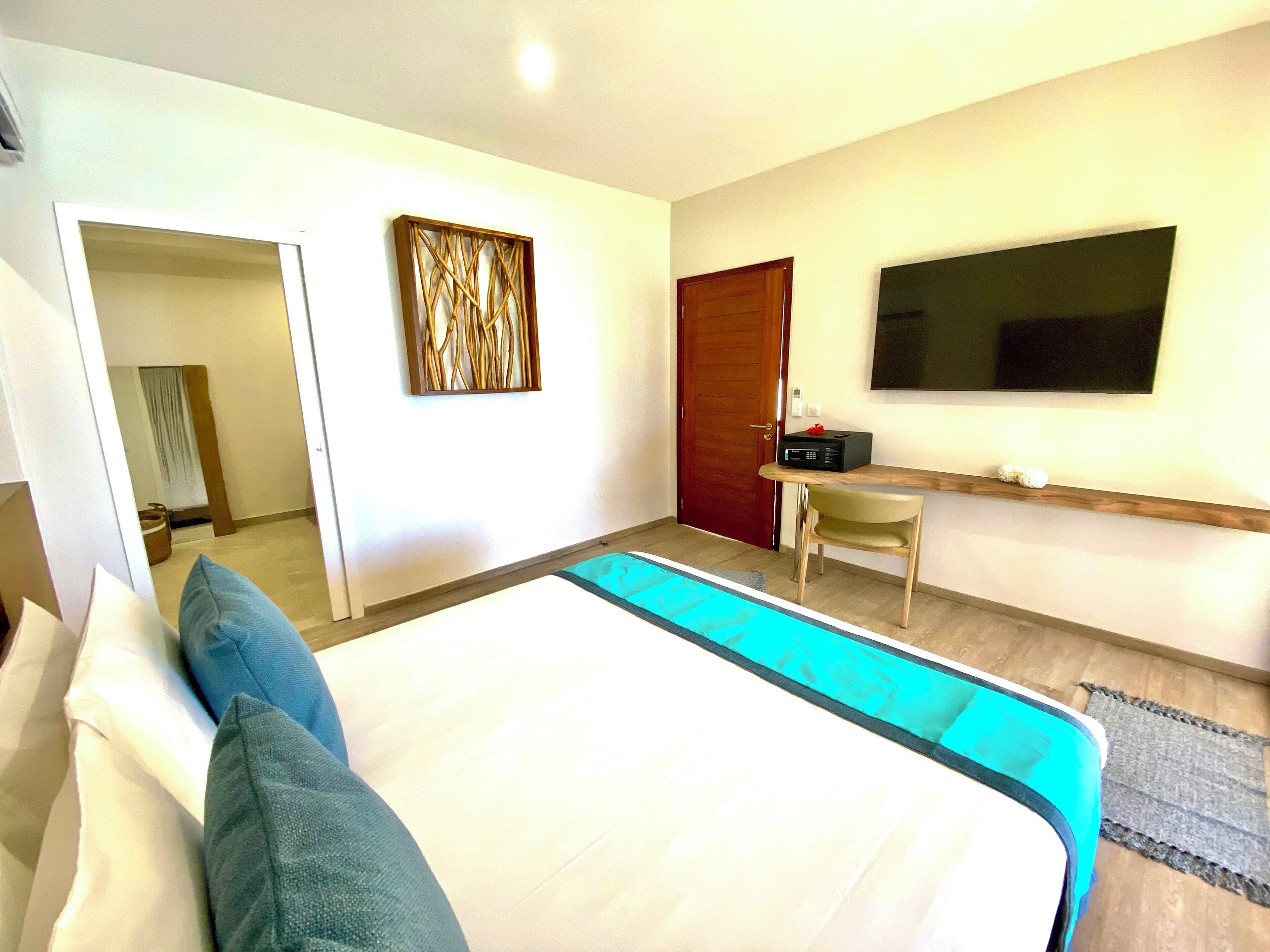 A modern hotel room with a large bed, a desk with a chair, a flat-screen TV, and a wooden door.