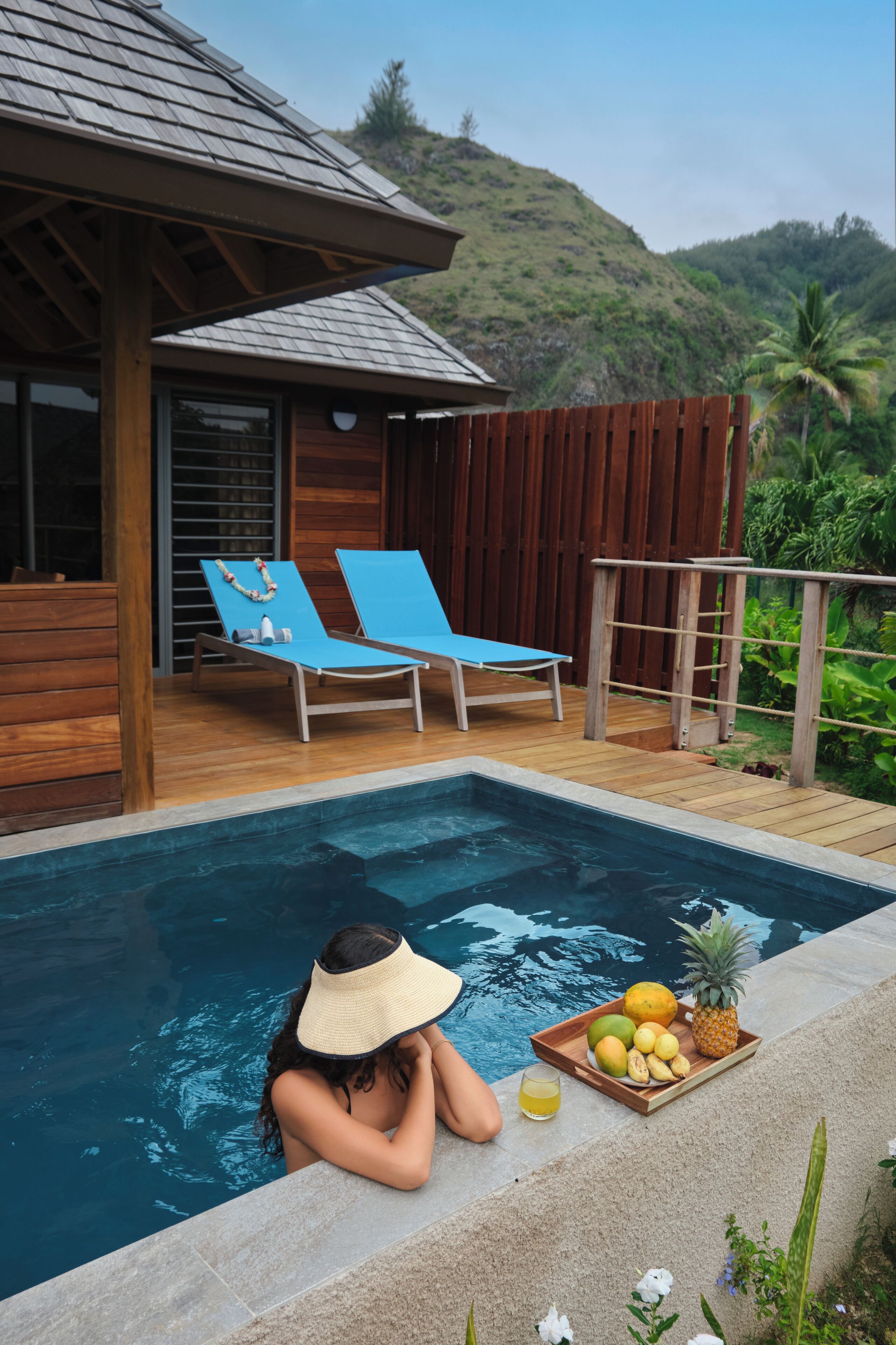 A poolside area with lounge chairs, a wooden deck, and a tropical view.