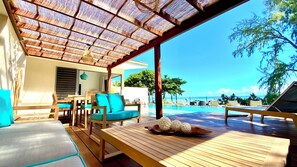 A covered outdoor seating area with wooden furniture and a view of the ocean. - Moorea Beach Villas (Moorea-Maiao)