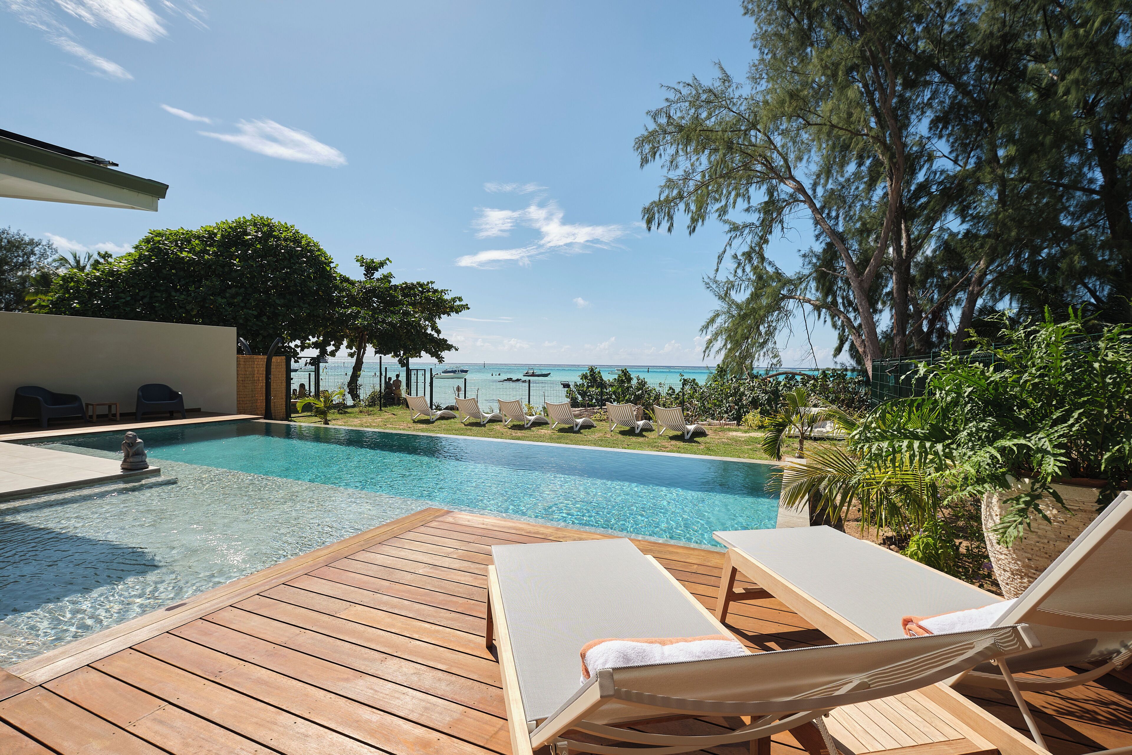 A wooden deck with lounge chairs and a swimming pool with a view of the ocean.