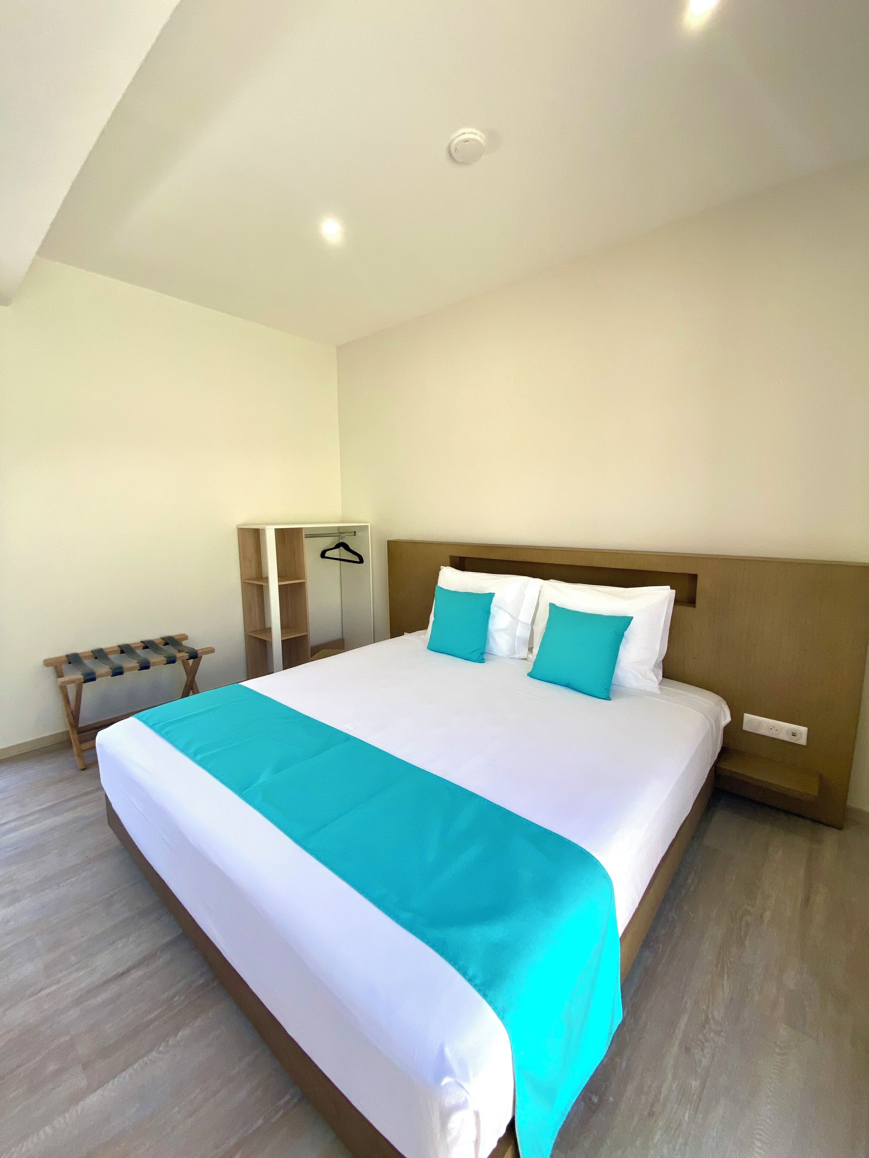 A neatly made bed with a white and teal bedspread, a wooden headboard, and a wooden bench with a towel rack beside it.
