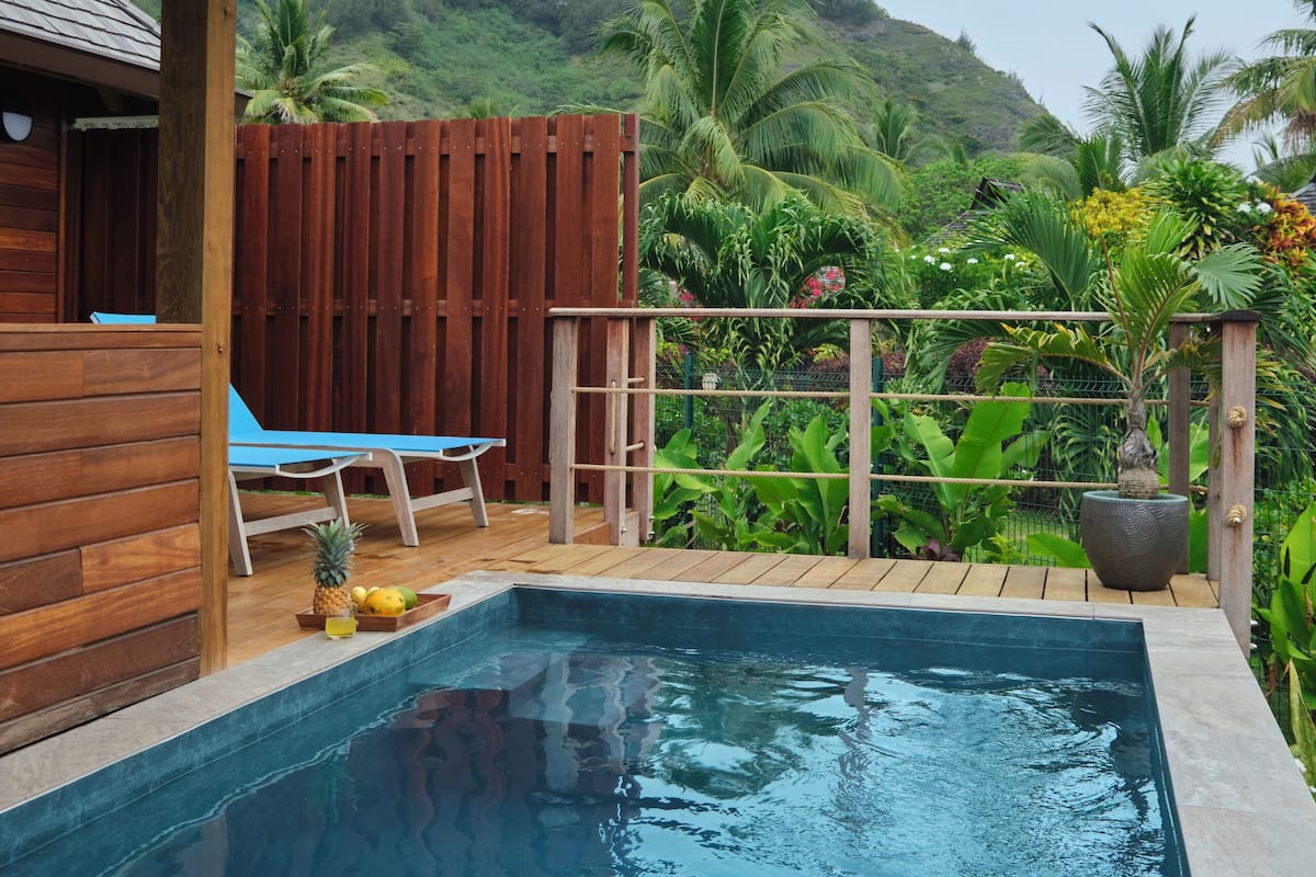 A pool area with wooden deck, lounge chairs, and a view of lush greenery and hills in the background.