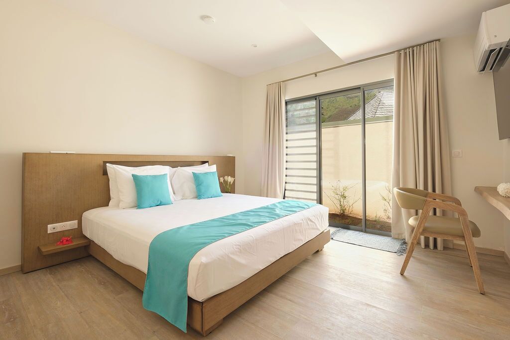 A modern hotel room with a large bed, a desk, and a sliding glass door leading to a balcony.