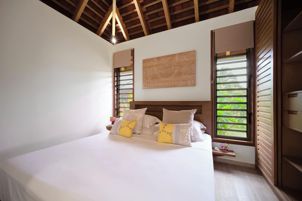 A bedroom with a large bed, wooden headboard, and a window with shutters.