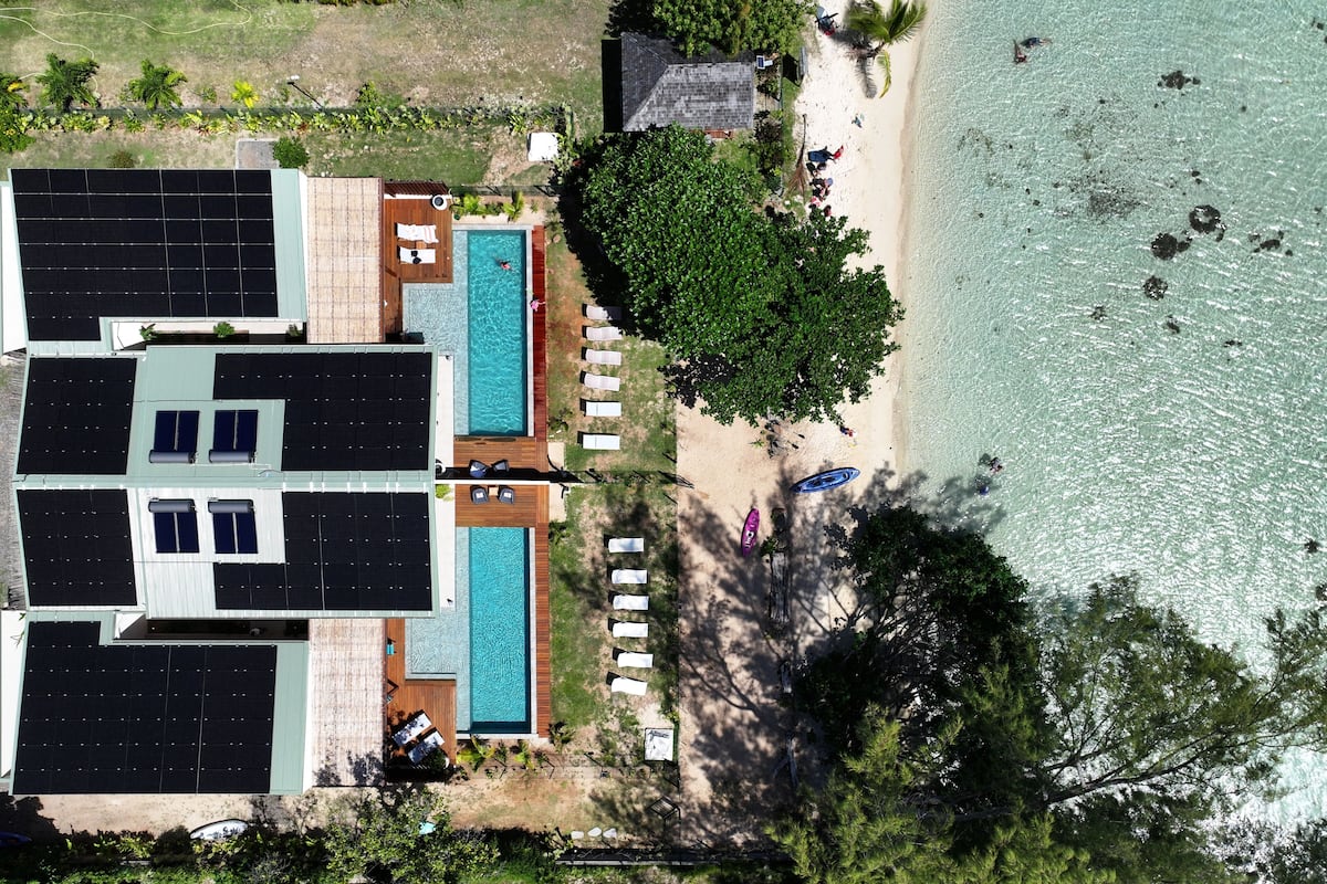 A large house with a swimming pool, a beach, and solar panels.