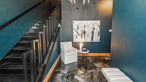 A modern interior with a staircase, a white armchair, a small table with a book, and a painting on the wall.