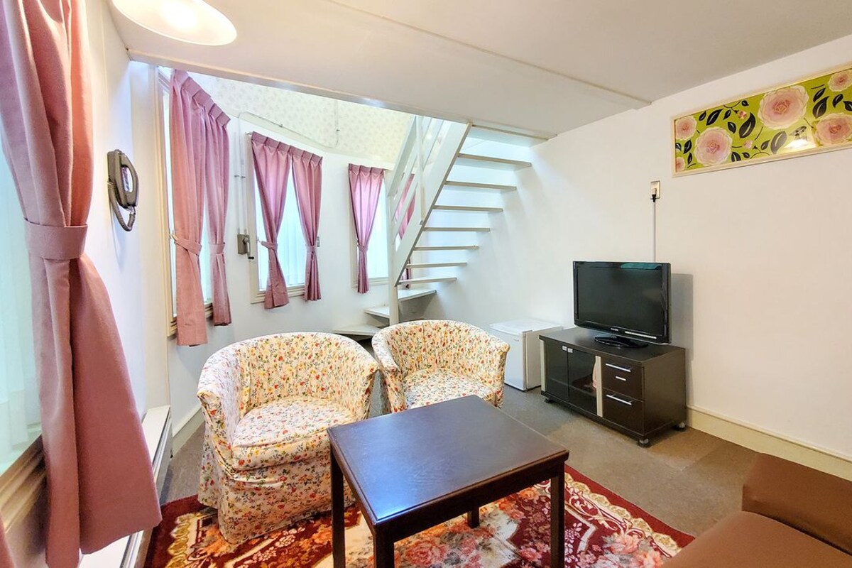 A living room with a staircase, a television, and floral-patterned chairs.