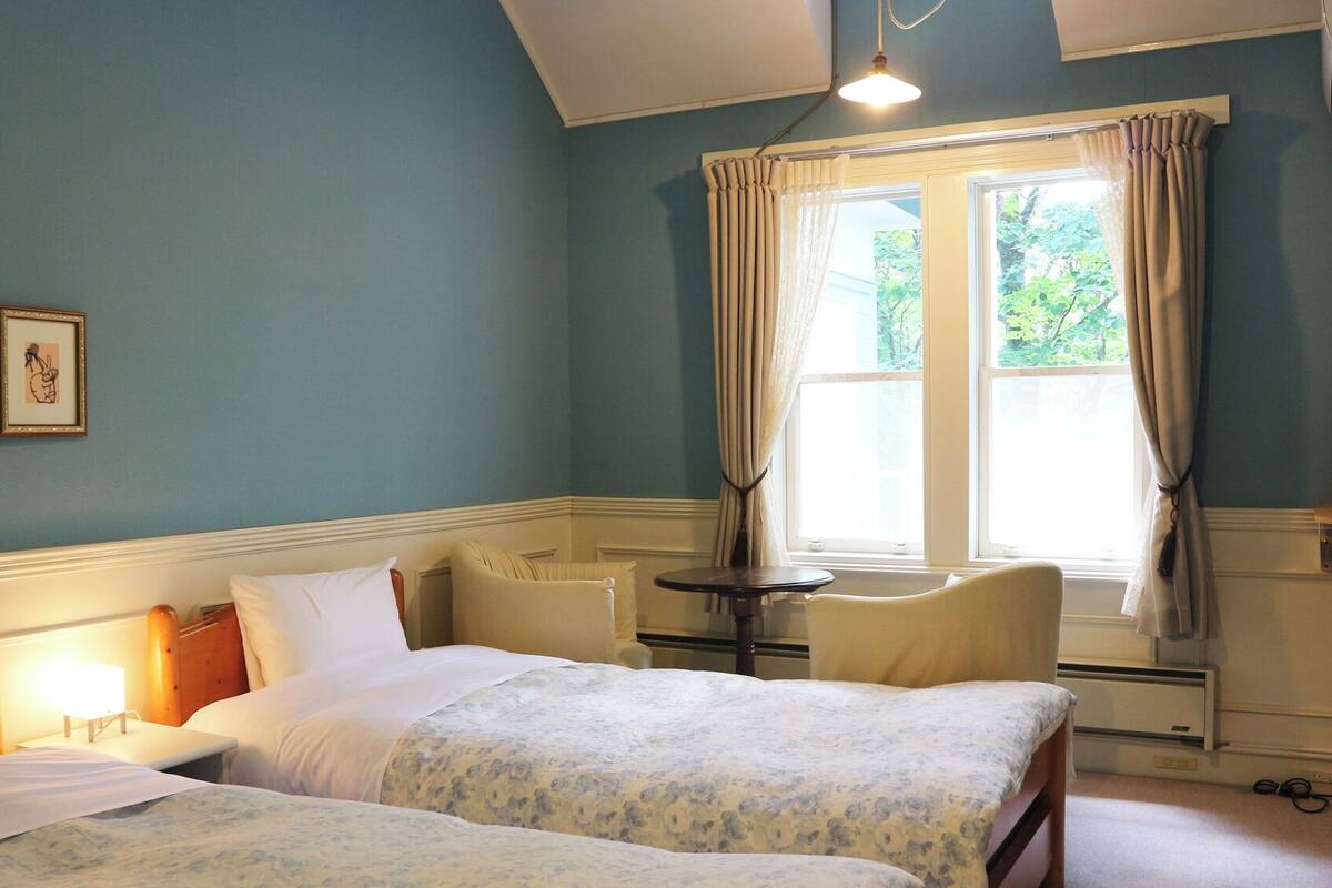 A hotel room with two beds, a small table, a TV, and a window with curtains.
