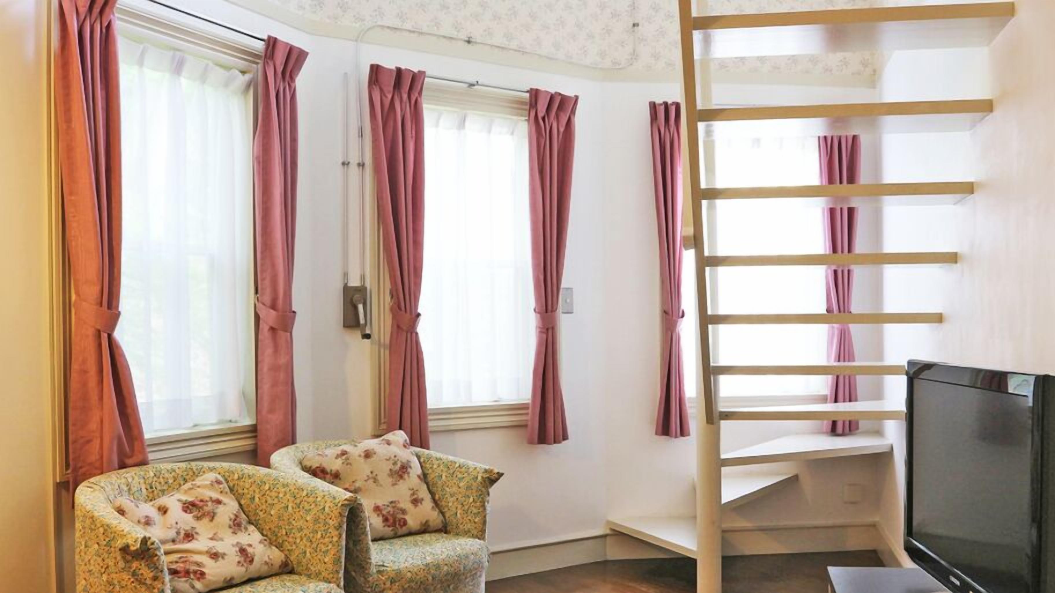 A room with a sofa, a TV, a staircase, and windows with curtains.