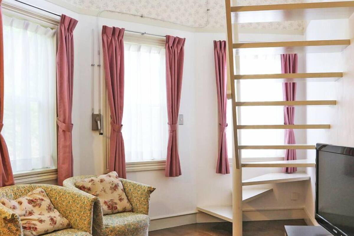 A room with a sofa, a TV, a staircase, and windows with curtains.