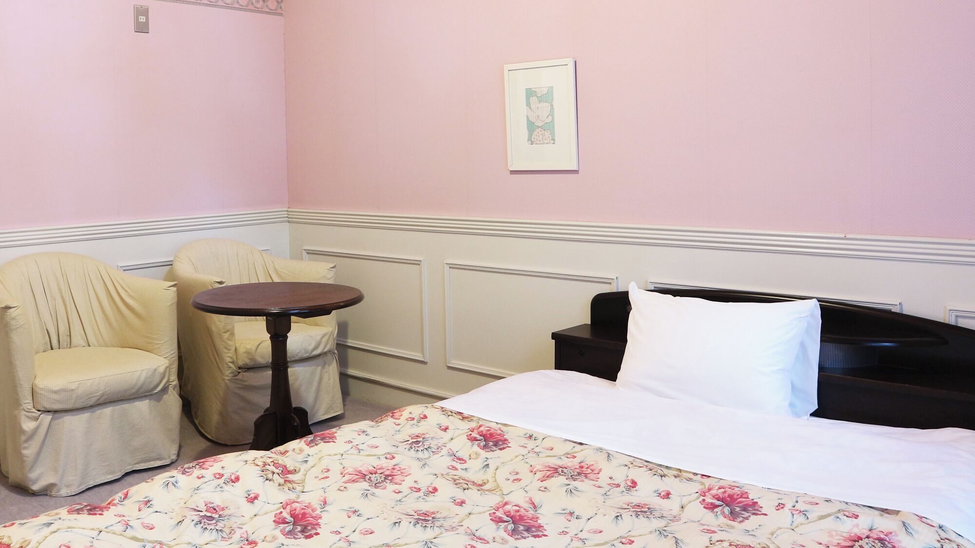 A room with a bed, two chairs, a small table, and a framed picture on the wall.