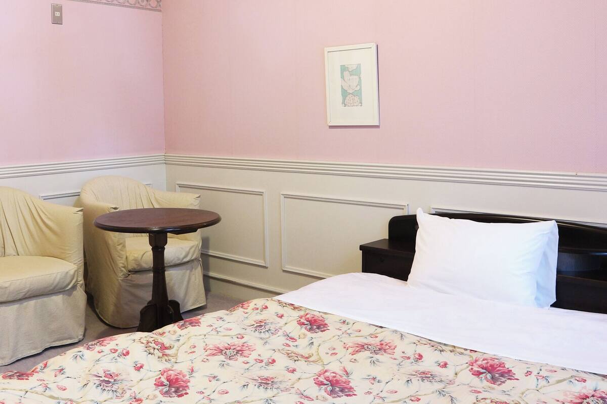 A room with a bed, two chairs, a small table, and a framed picture on the wall.