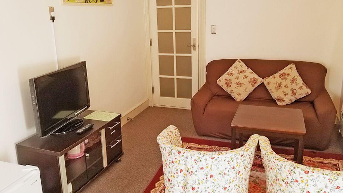 A living room with a sofa, a small table, a TV on a cabinet, and a door with a glass panel.