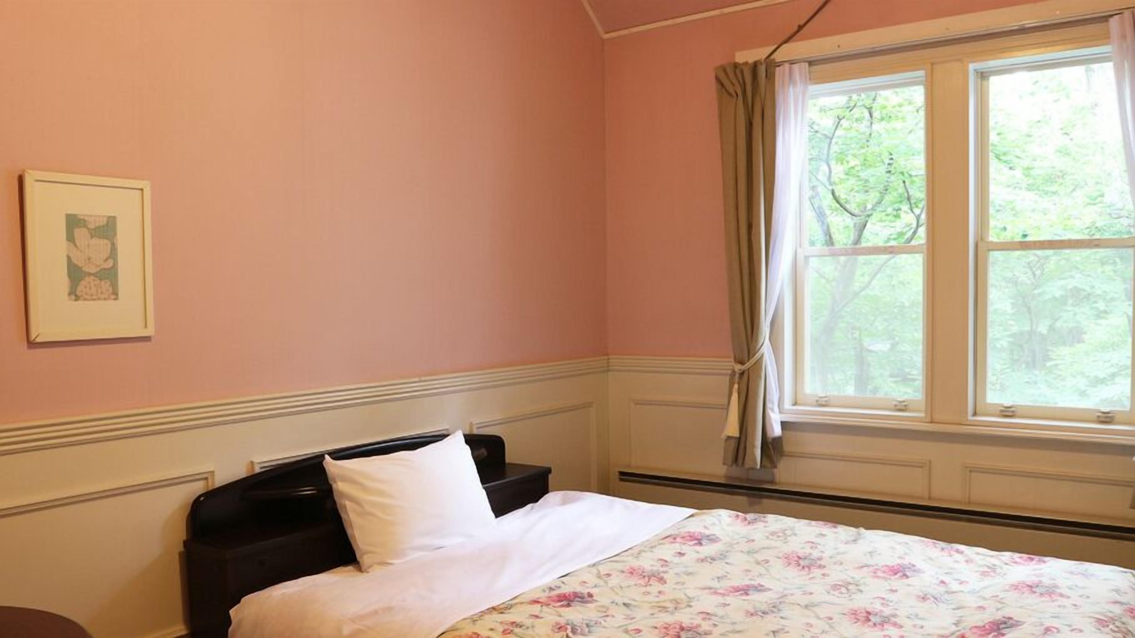 A bedroom with a bed, a window with curtains, a framed picture on the wall, and a floral bedspread.