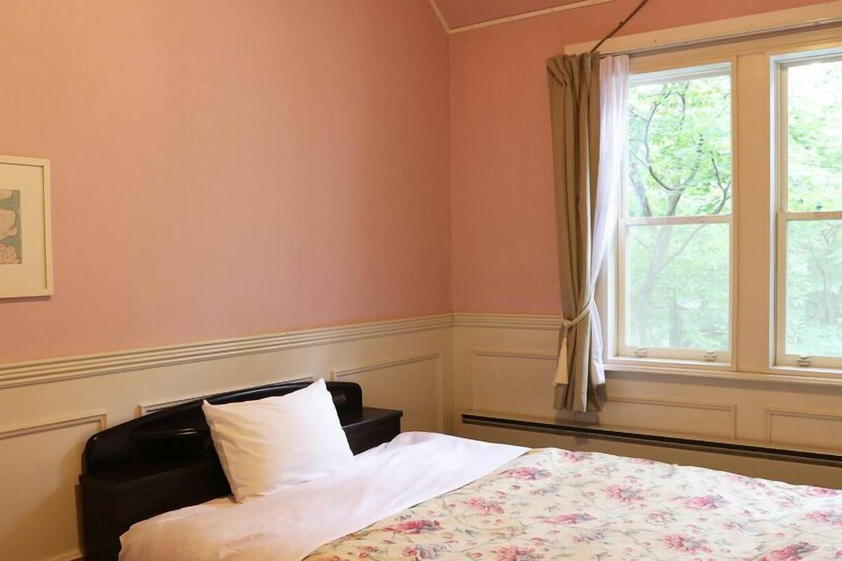 A bedroom with a bed, a window with curtains, a framed picture on the wall, and a floral bedspread.
